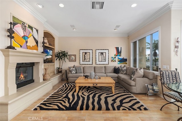 living area featuring ornamental molding, visible vents, wood finished floors, and a glass covered fireplace