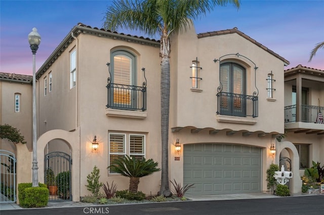 mediterranean / spanish house featuring an attached garage, driveway, stucco siding, and a balcony