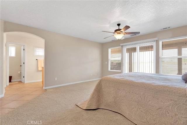 bedroom featuring a textured ceiling, arched walkways, light carpet, baseboards, and visible vents