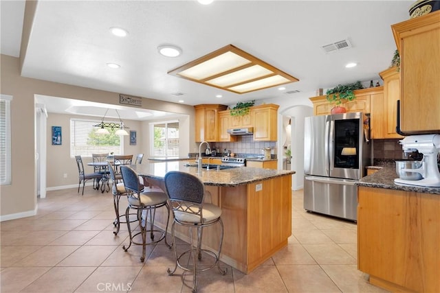 kitchen featuring stainless steel appliances, a sink, light tile patterned floors, a kitchen bar, and tasteful backsplash