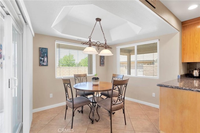 dining area with baseboards, light tile patterned flooring, a tray ceiling, and plenty of natural light