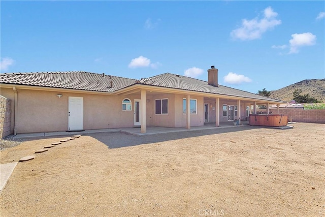 rear view of property featuring a chimney, stucco siding, a patio area, a hot tub, and a mountain view