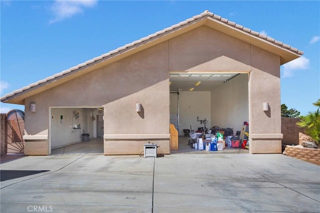 rear view of house with fence, a tiled roof, a garage, and stucco siding