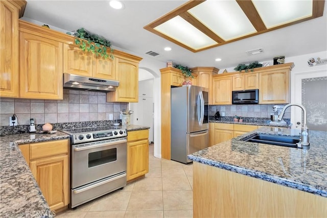 kitchen with a sink, stainless steel appliances, stone counters, under cabinet range hood, and visible vents