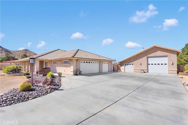 ranch-style house featuring driveway, a tiled roof, a mountain view, a garage, and stucco siding