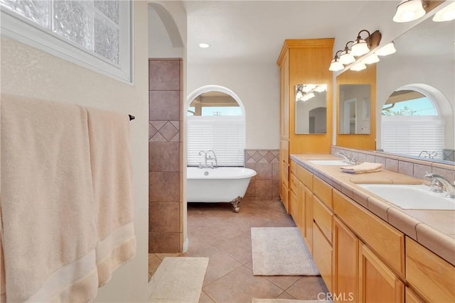 bathroom with tile patterned floors, a sink, double vanity, tile walls, and a freestanding tub