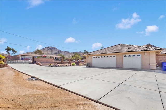 view of front facade featuring fence, a tiled roof, concrete driveway, stucco siding, and a mountain view