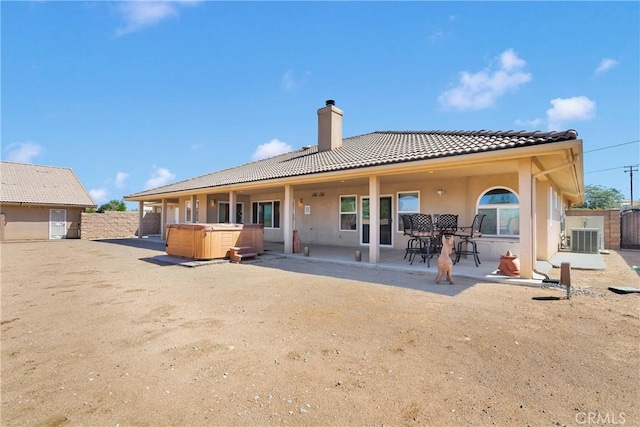 rear view of house with a chimney, a tiled roof, stucco siding, a patio area, and a hot tub