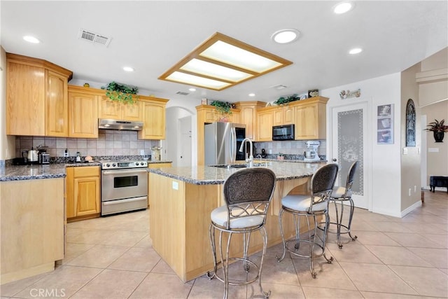 kitchen featuring under cabinet range hood, tasteful backsplash, stainless steel appliances, and light tile patterned flooring