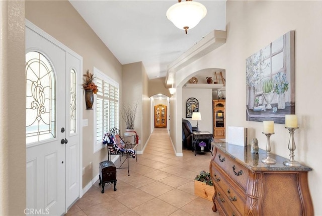 foyer entrance with baseboards, arched walkways, and light tile patterned floors