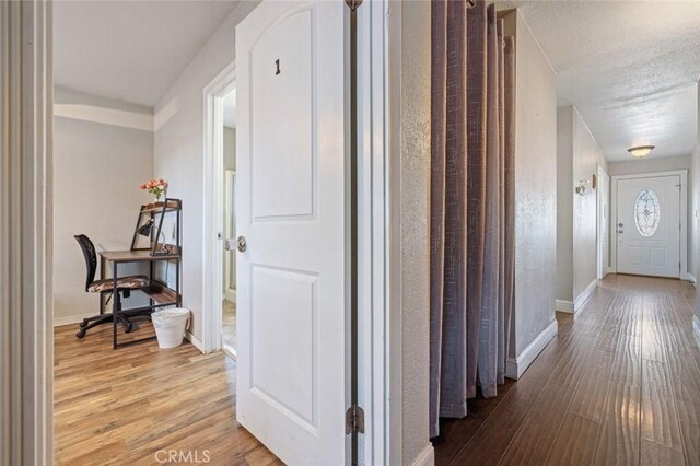hall featuring light wood finished floors, baseboards, and a textured ceiling