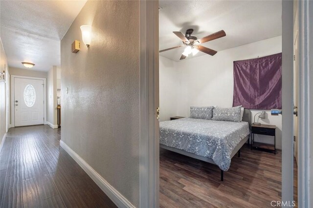 bedroom featuring ceiling fan, wood finished floors, baseboards, and a textured wall