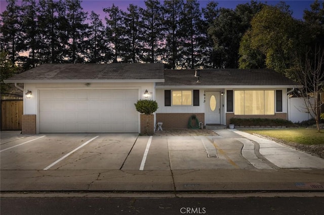 ranch-style house with fence, a shingled roof, an attached garage, driveway, and brick siding