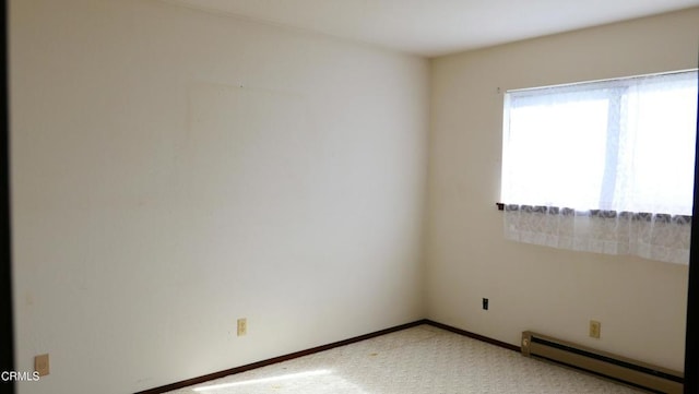 spare room with a baseboard heating unit, light carpet, and baseboards