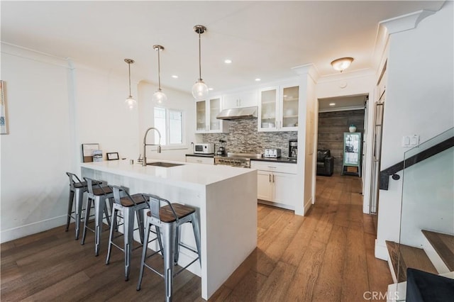 kitchen featuring a kitchen breakfast bar, a sink, glass insert cabinets, a peninsula, and under cabinet range hood