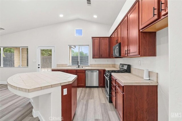 kitchen with vaulted ceiling, tile counters, stainless steel appliances, and light wood-style floors