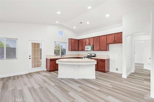 kitchen with a sink, light wood-style floors, light countertops, a kitchen island, and appliances with stainless steel finishes