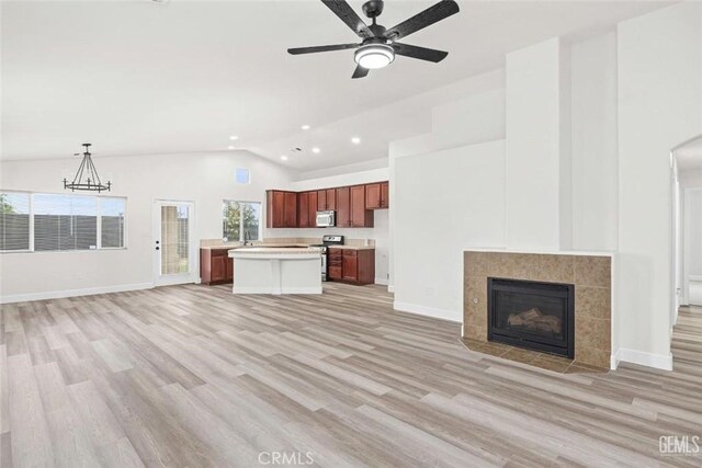 unfurnished living room with recessed lighting, vaulted ceiling, light wood-style floors, a tiled fireplace, and ceiling fan with notable chandelier