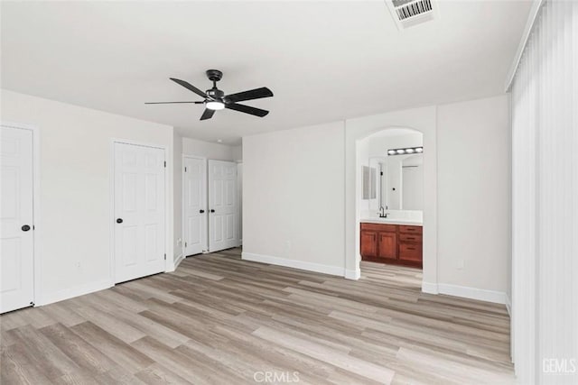 unfurnished bedroom featuring visible vents, arched walkways, baseboards, light wood-style flooring, and two closets