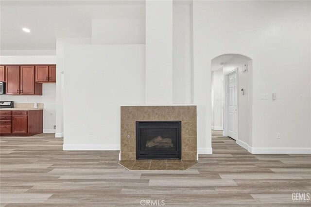 unfurnished living room with light wood-style floors, arched walkways, a tile fireplace, baseboards, and recessed lighting