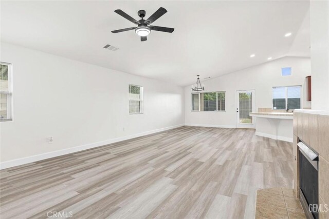 unfurnished living room with light wood finished floors, a tiled fireplace, visible vents, vaulted ceiling, and a ceiling fan