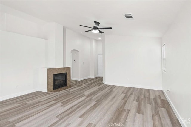 unfurnished living room featuring a tile fireplace, wood finished floors, visible vents, a ceiling fan, and arched walkways