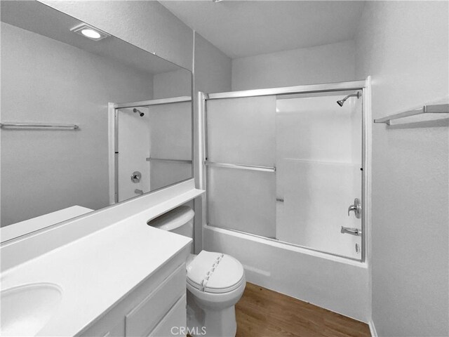 full bathroom with enclosed tub / shower combo, toilet, vanity, and wood finished floors