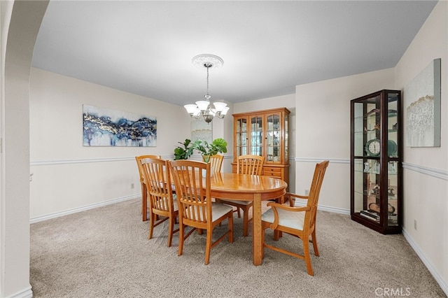 dining room featuring arched walkways, baseboards, light carpet, and an inviting chandelier