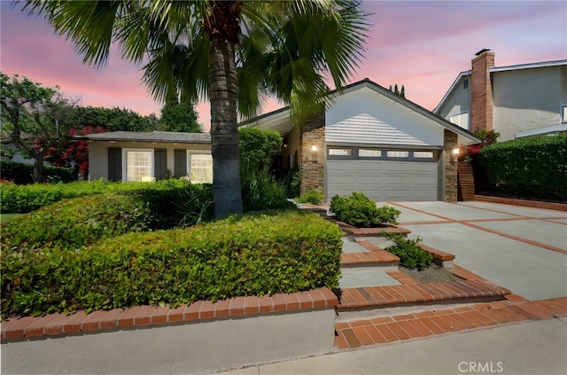 single story home with an attached garage, stone siding, and concrete driveway