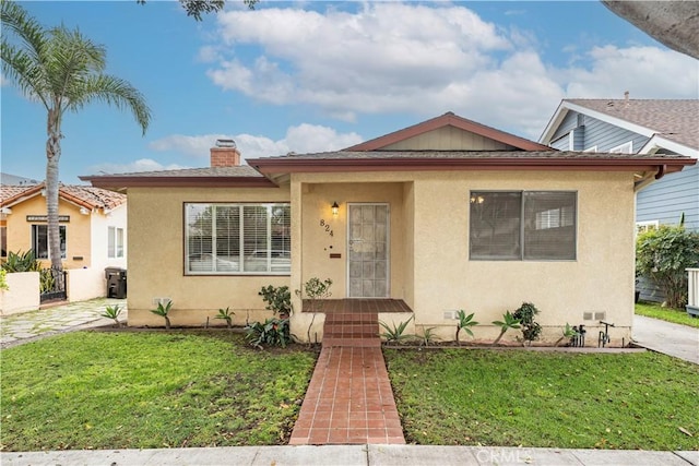 bungalow-style home with a chimney, a front yard, and stucco siding