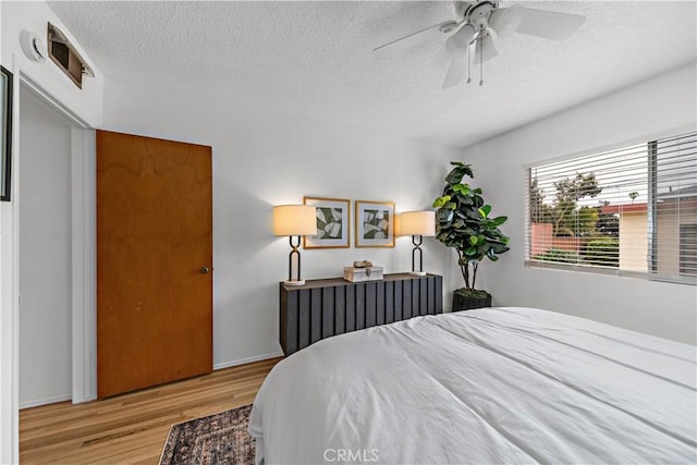 bedroom featuring a ceiling fan, visible vents, wood finished floors, and a textured ceiling