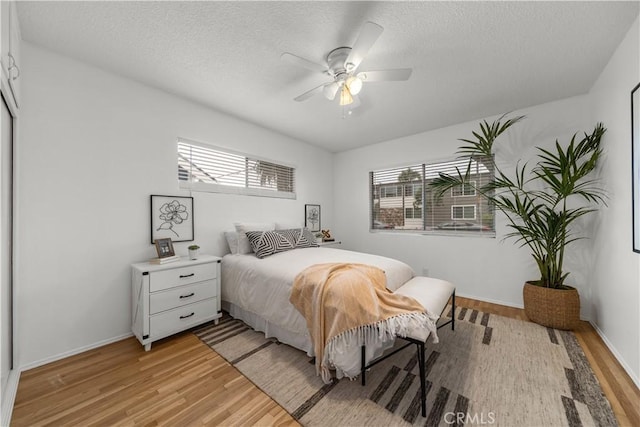 bedroom with baseboards, multiple windows, a textured ceiling, and light wood-style flooring