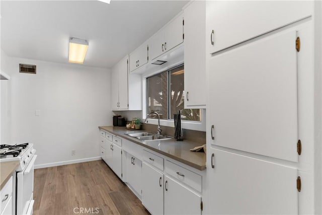 kitchen with a sink, light wood-type flooring, baseboards, white gas stove, and white cabinetry