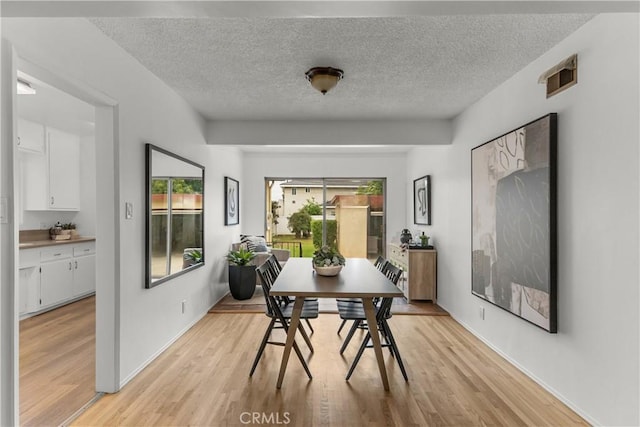 dining room featuring light wood-style floors, baseboards, visible vents, and a textured ceiling