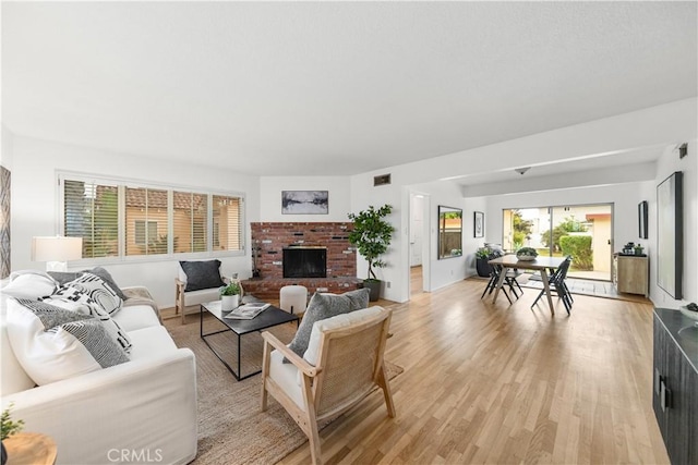 living area with light wood-style floors, a brick fireplace, and visible vents