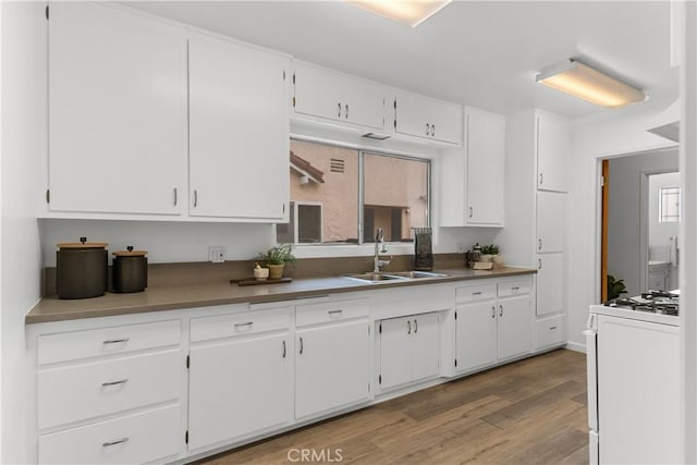 kitchen with white cabinets, white gas stove, a sink, and light wood-type flooring