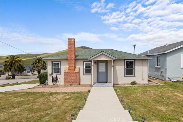 view of front of house with a front lawn, a shingled roof, stucco siding, and a chimney