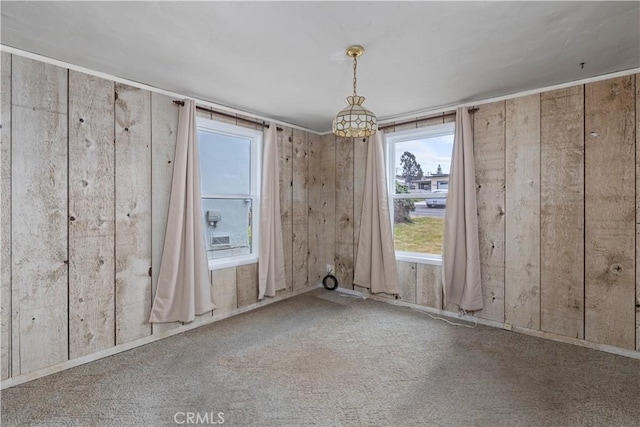 unfurnished dining area with wood walls, a wealth of natural light, and carpet flooring