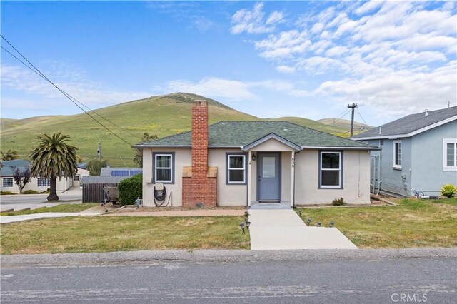 view of front of property featuring roof with shingles, a mountain view, stucco siding, a front lawn, and a chimney