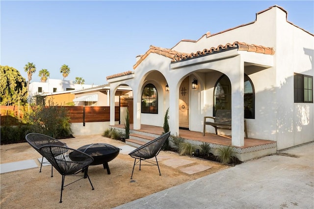 rear view of house with fence, a tiled roof, stucco siding, covered porch, and an outdoor fire pit