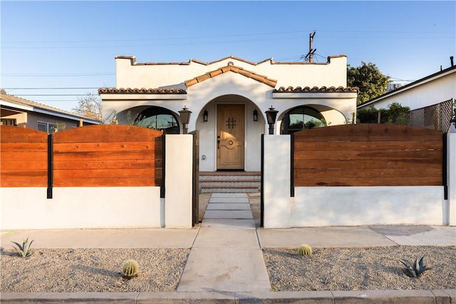 mediterranean / spanish home with a gate, a fenced front yard, a tiled roof, and stucco siding