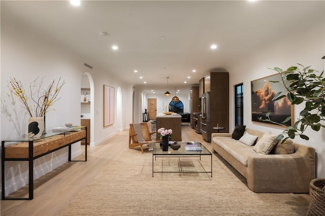 living room featuring recessed lighting, arched walkways, and light wood-style floors