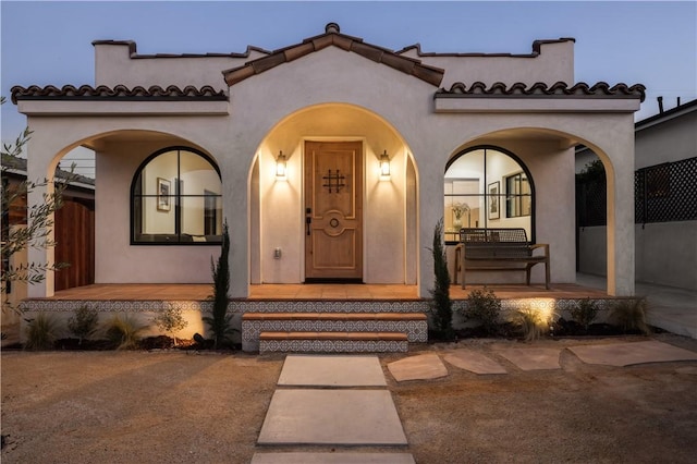 entrance to property featuring stucco siding, a tile roof, and a porch