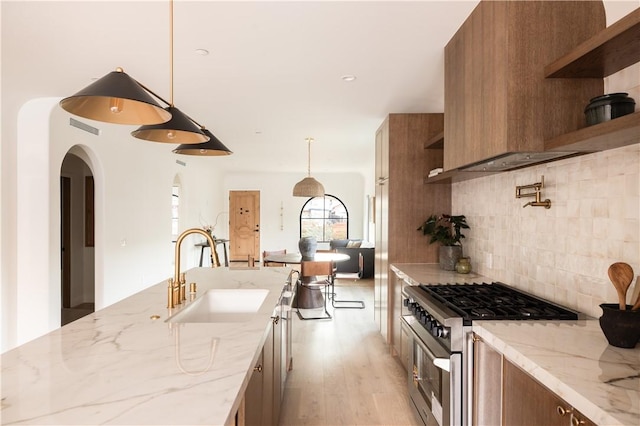 kitchen with open shelves, brown cabinetry, stainless steel range, and a sink