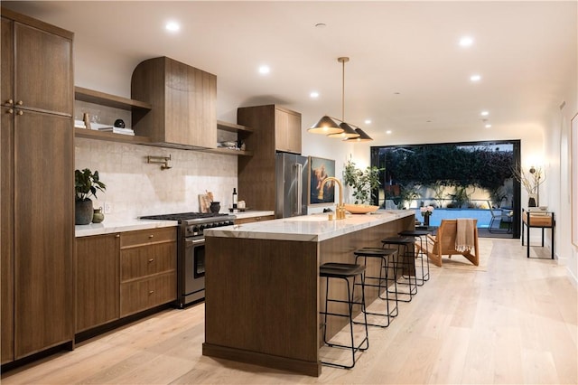 kitchen featuring a kitchen island with sink, a sink, premium appliances, open shelves, and a breakfast bar area