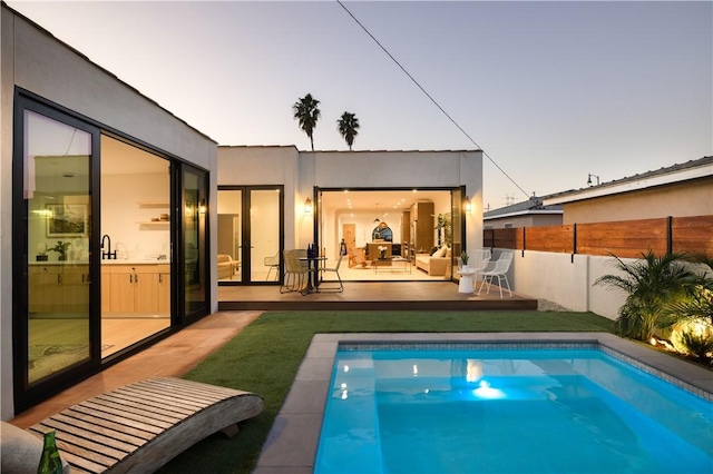 rear view of property featuring stucco siding, fence, a patio, and a fenced in pool
