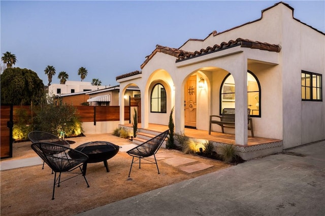 rear view of property featuring stucco siding, covered porch, a tile roof, and an outdoor fire pit
