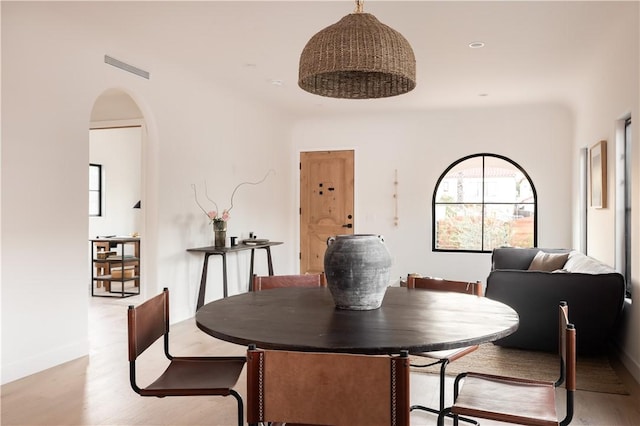 dining area featuring arched walkways, wood finished floors, visible vents, and a healthy amount of sunlight