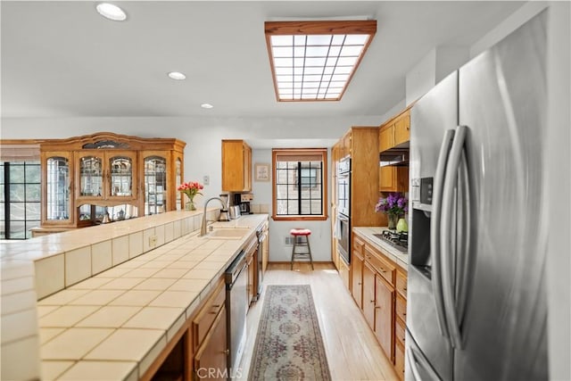 2116 Ironwood Ct, Pine Mountain Club, CA 93222 - kitchen with appliances with stainless steel finishes, tile countertops, a sink, light wood finished floors, and exhaust hood
