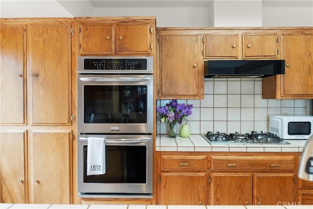 2116 Ironwood Ct, Pine Mountain Club, CA 93222 - kitchen with tasteful backsplash, brown cabinetry, under cabinet range hood, tile countertops, and appliances with stainless steel finishes